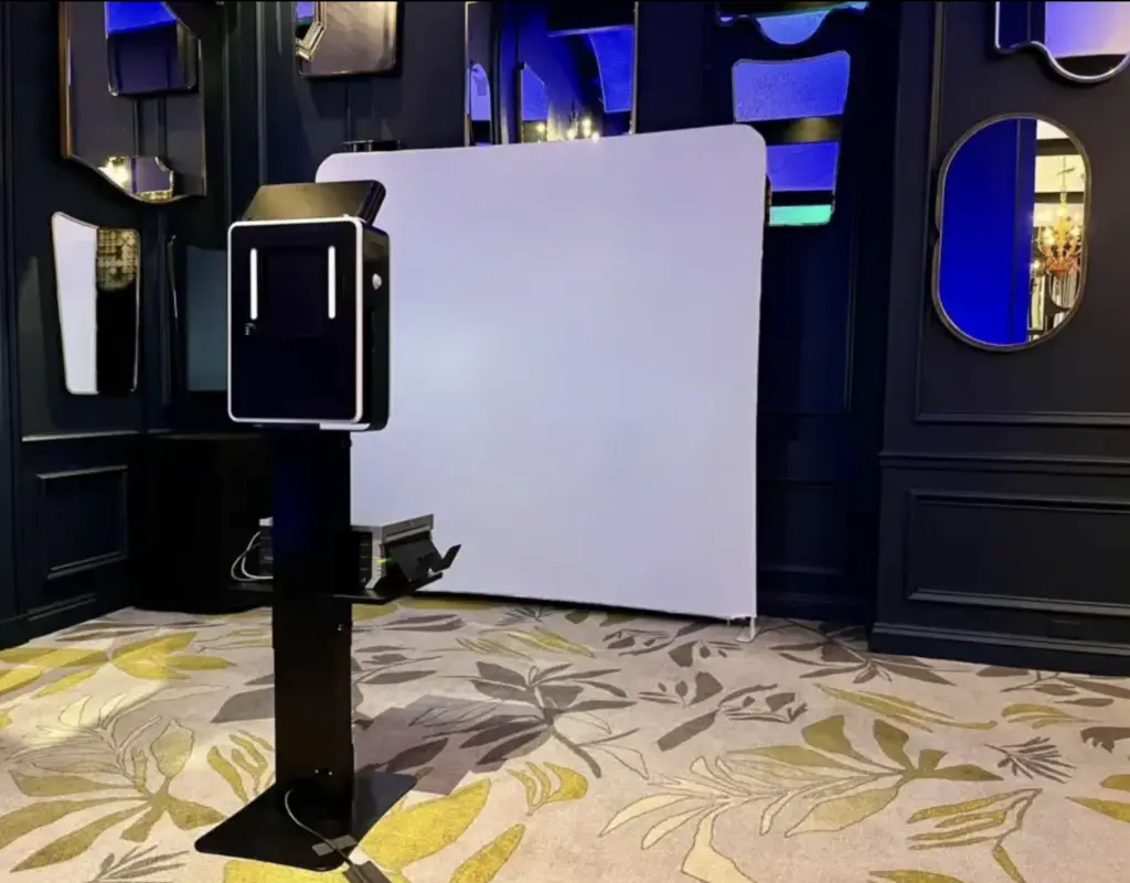 Three branded photo booth towers featuring pink, black, and white designs with prominent logos and text.