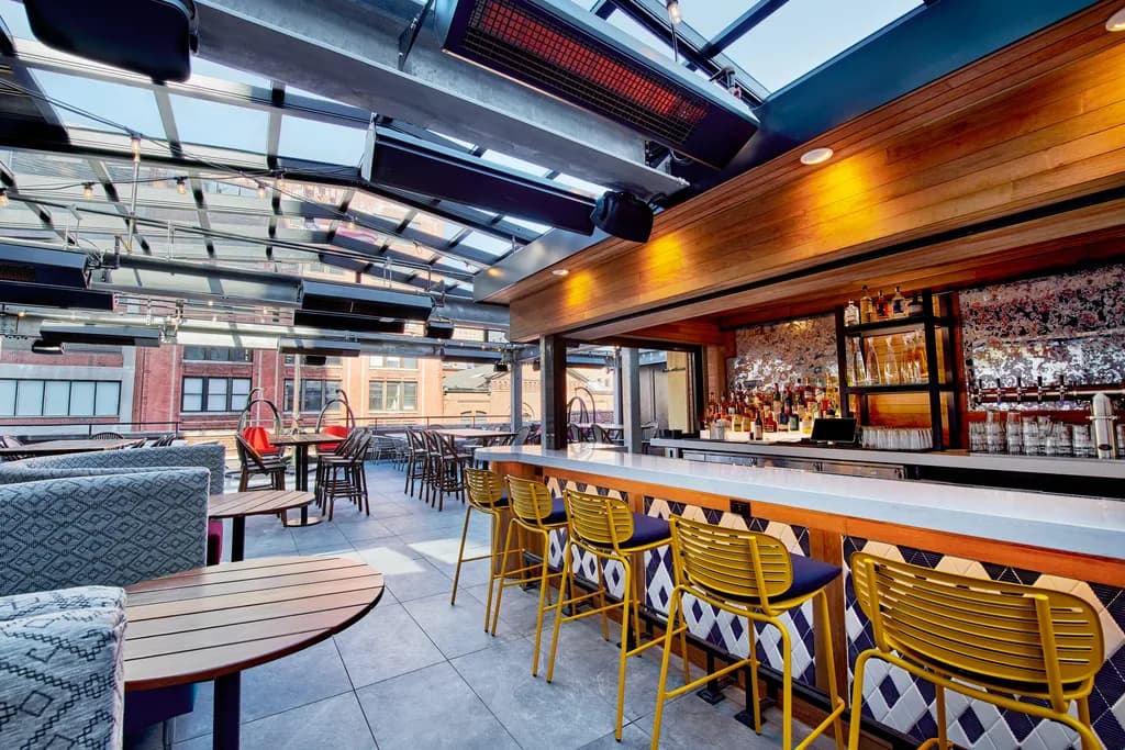 Modern rooftop bar with retractable roof and vibrant bar stools.
