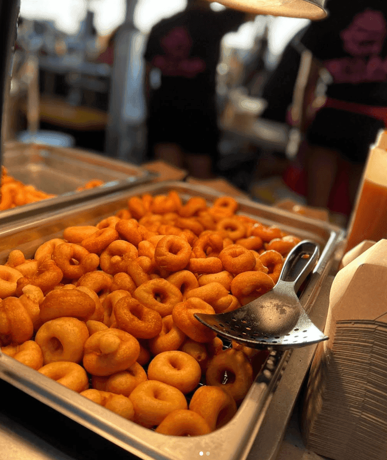 A tray filled with freshly made mini donuts, with a slotted serving spoon resting on the edge.