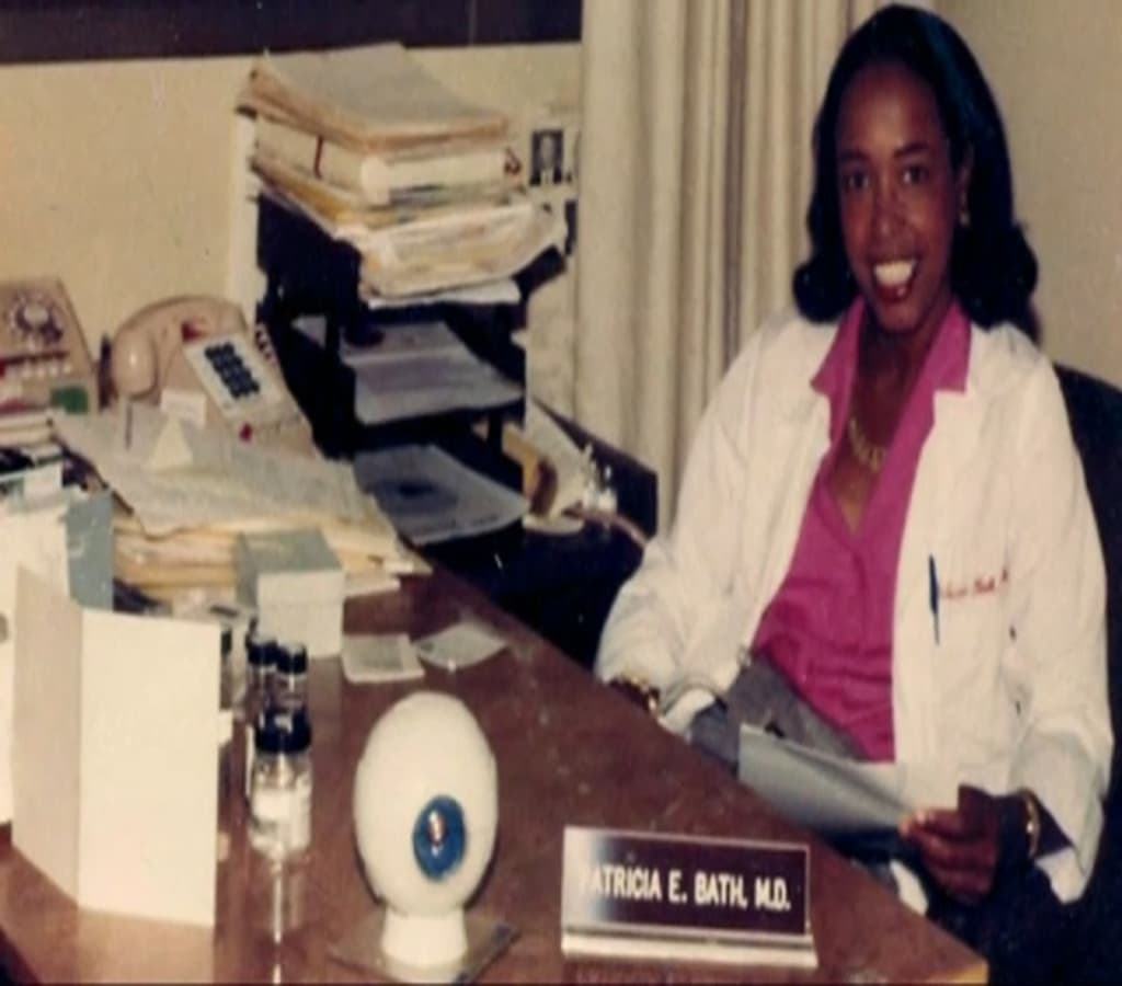 Dr. Patricia E. Bath, M.D., sits at her desk filled with papers and medical models, showcasing her groundbreaking contributions to ophthalmology.