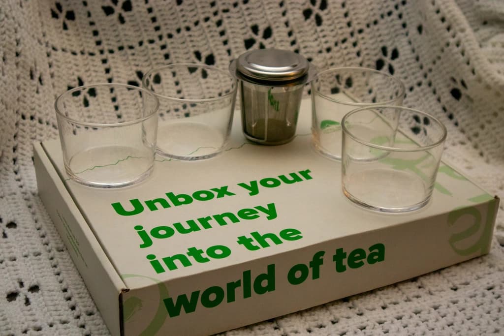 Kit with glasses and a tea infuser, labeled 'Unbox your journey into the world of tea' on the box.
