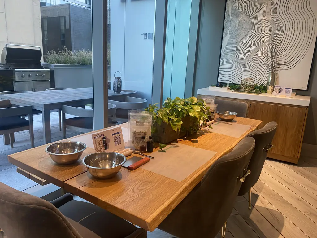 A modern kitchen setup for a dumpling-making workshop with bowls, ingredients, and utensils on a wooden table near a patio with a grill.